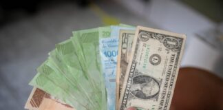 Una mano sostiene un dólar americano para compararlo con los billetes de bolívares venezolanos